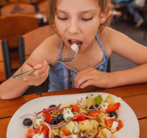 Child eating Greek salad at a Greek restaurant. Greece holidays for kids.